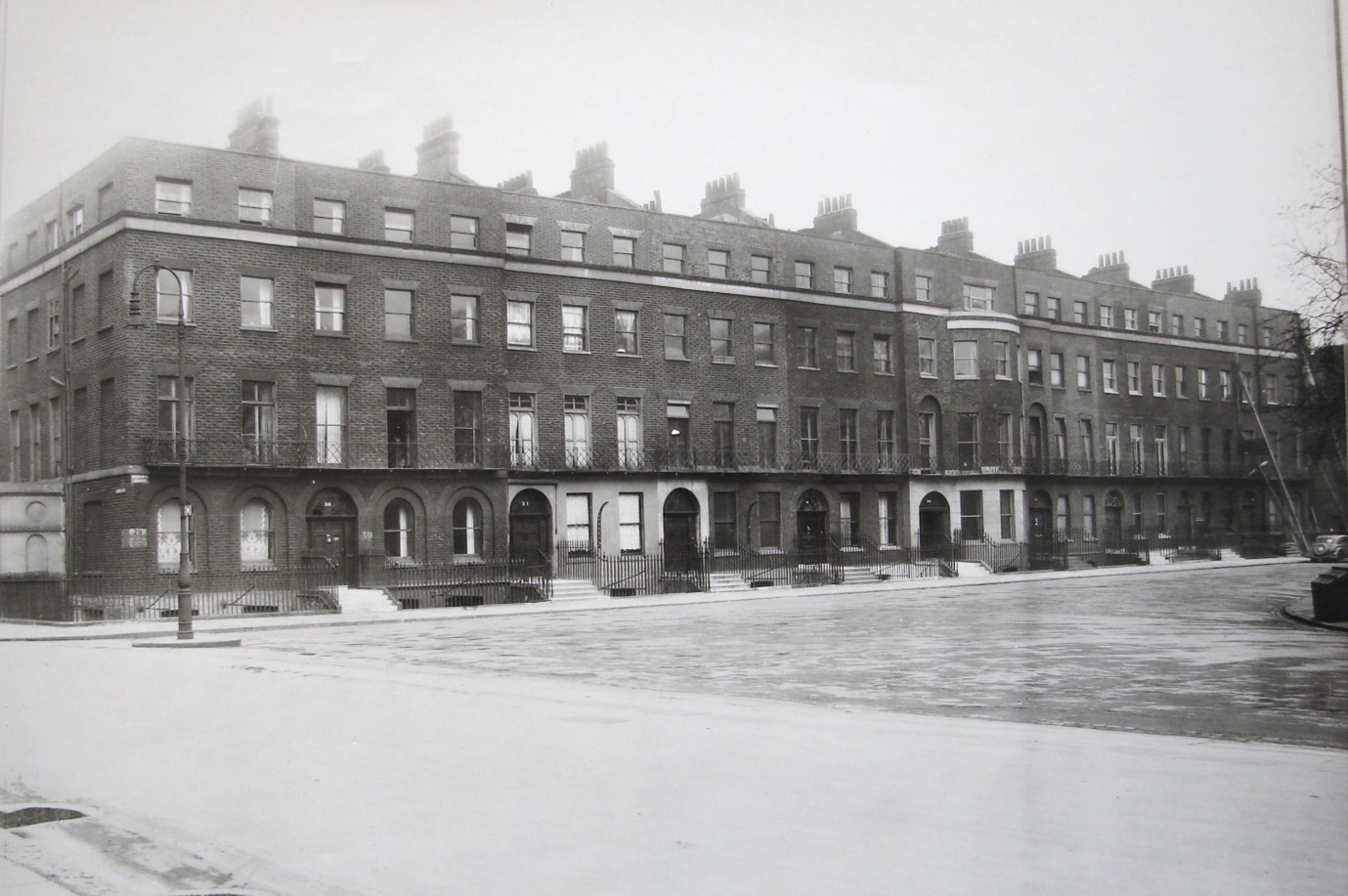 Black and white photo of a block of terraced 5 storey housing with snow on the ground. 
