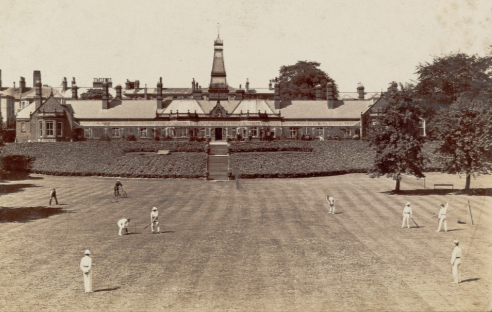 black and white photo of cricketers on a field in front of a large ornate building