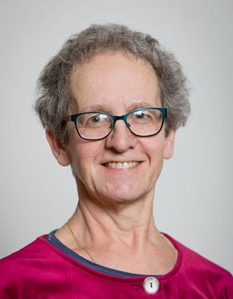 Older, smiling, white woman with short, curly, grey hair and glasses