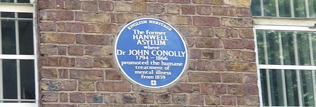 Blue plaque on brick wall, reading: English Heritage, The former Hanwell Asylum where Dr John Connolly 1794-1866 promoted the humane treatment of mental illness from 1839. 