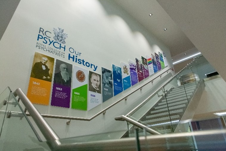 Staircase with brightly coloured posters at intervals up the wall, the College logo and the title: Our History.