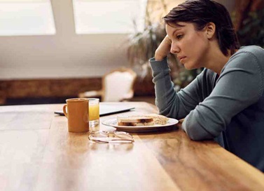 Young women sitting at wooden table with sandwich on a plate and orange juice in front of her.